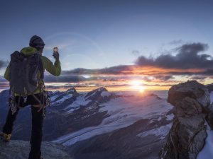 Mountaineer taking a picture of the sunset on their phone